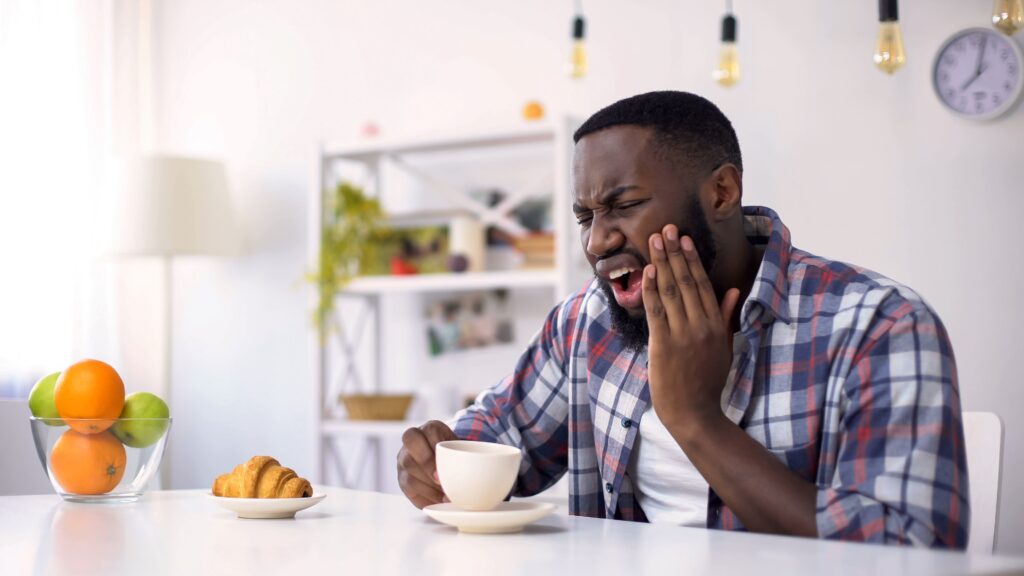 A man sitting at a table holding his jaw from tooth pain.