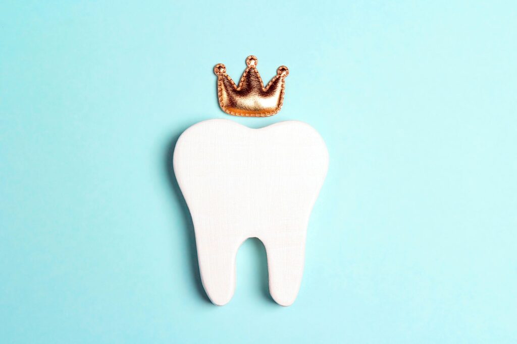 Flat white toy tooth on a light blue surface with a small gold crown above it